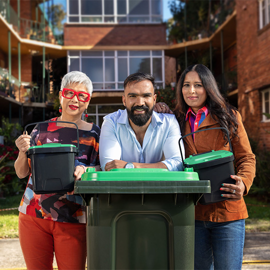 Three residents holding FOGO benchtop bins in front of an apartment